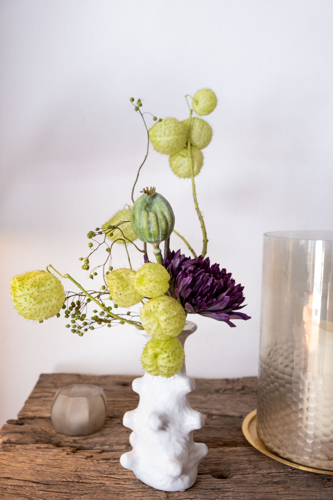 Un bouquet de fleur vert et violet avec un vase blanc et table en bois